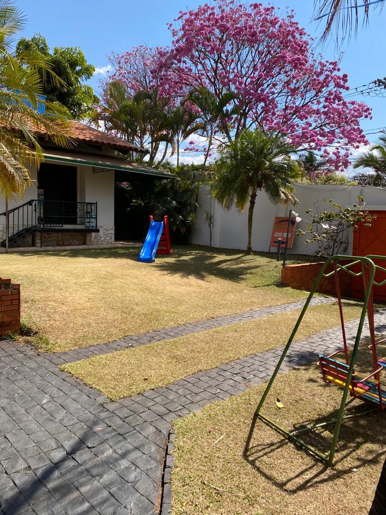 Jardim com ipê rosa florido, gramado, escorregador e balanço