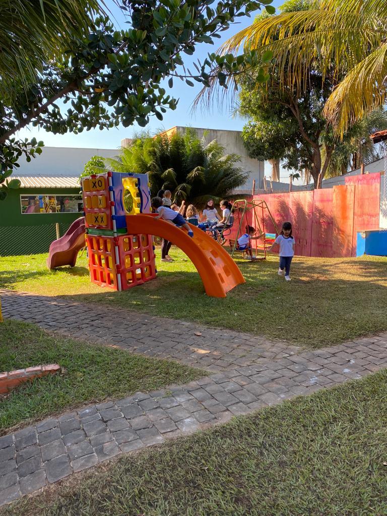 Crianças brincando no parque com escorregador laranja e balanço
